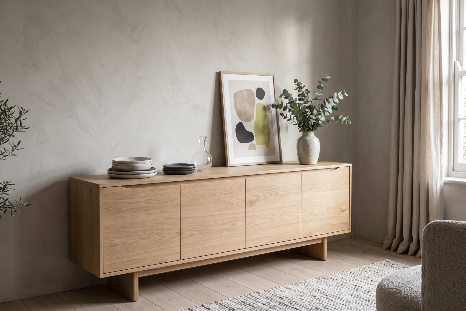 Light oak sideboard styled with handmade plates, a carafe and a vase of eucalyptus